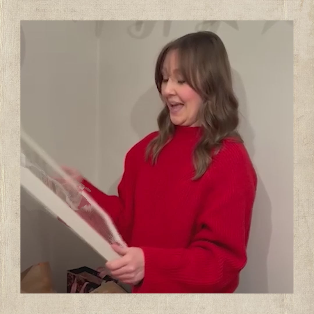 A customer unwrapping a framed personalised newspaper poster and reacting to it